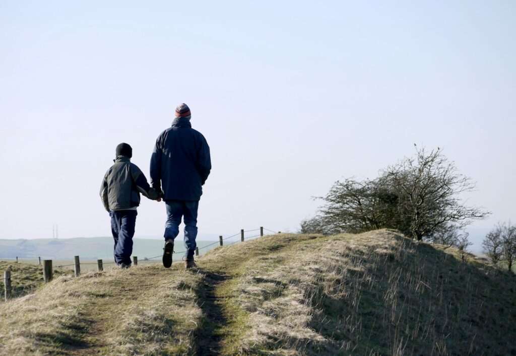 Adulto e menino caminhando lado a lado em uma trilha, vistos de costas